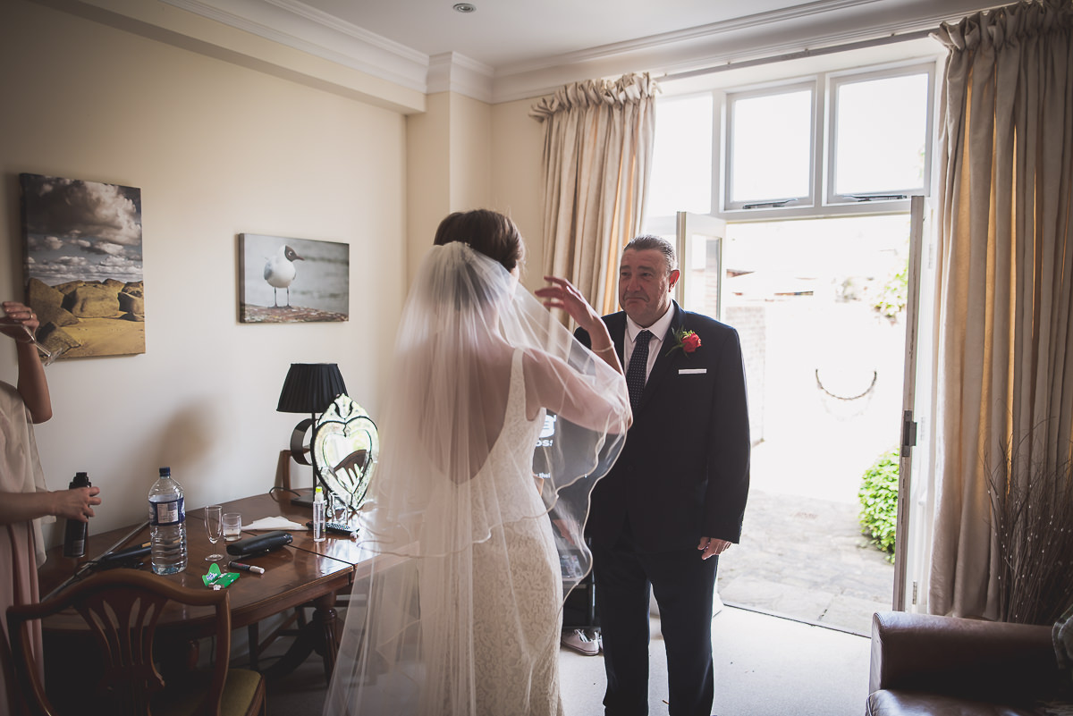 A bride is getting ready in a room with her father and wedding photographer.