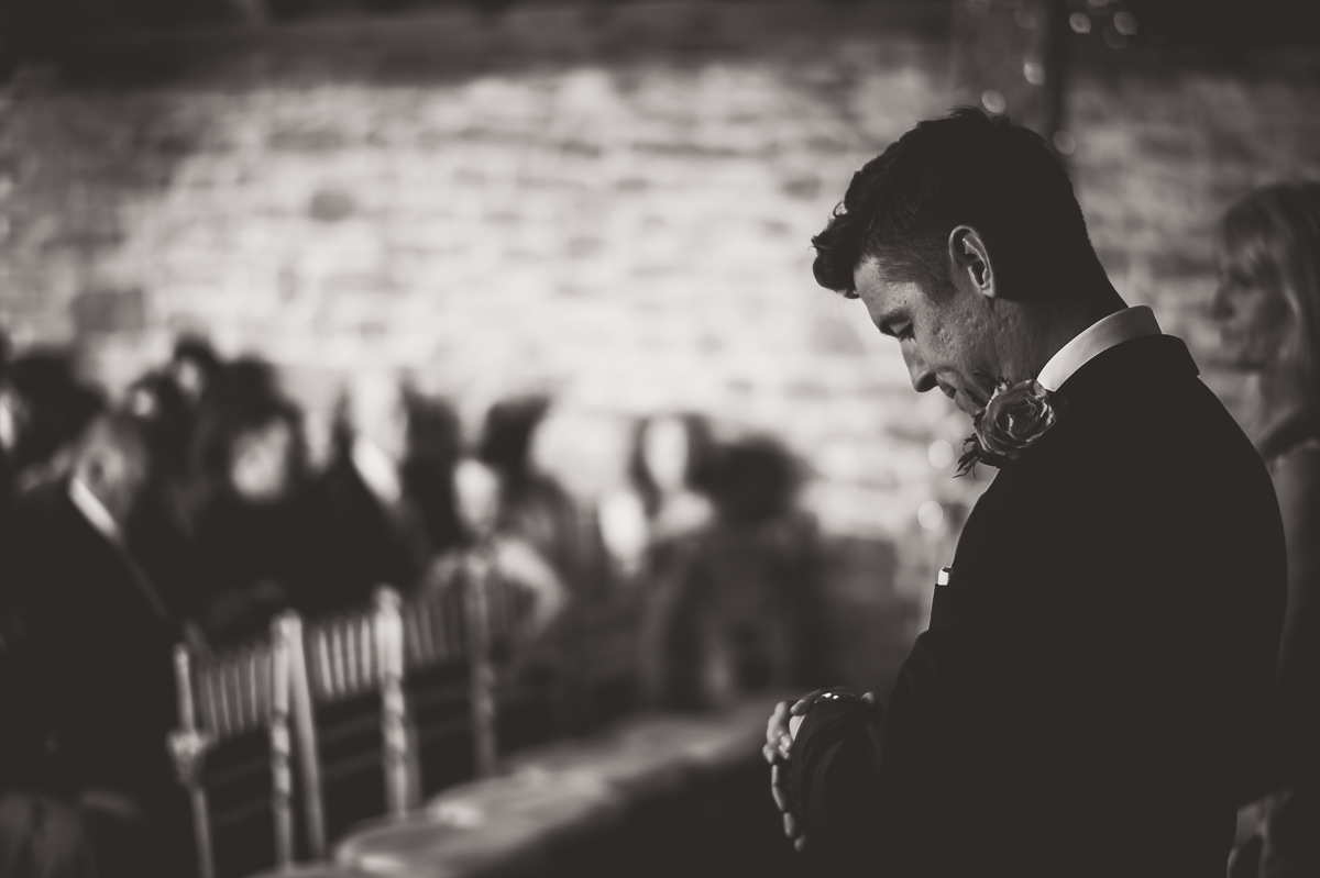 A wedding photographer captures a black and white photo of the groom at a ceremony.