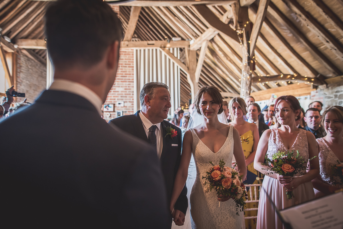 A groom and bride captured by a wedding photographer while walking down the aisle in a barn.