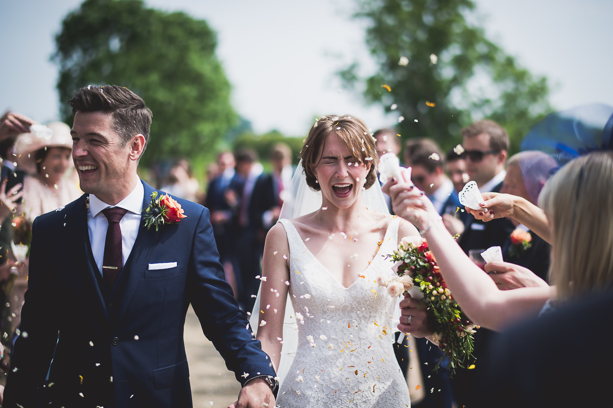 A wedding photographer captures bride and groom walking down the aisle amidst confetti.