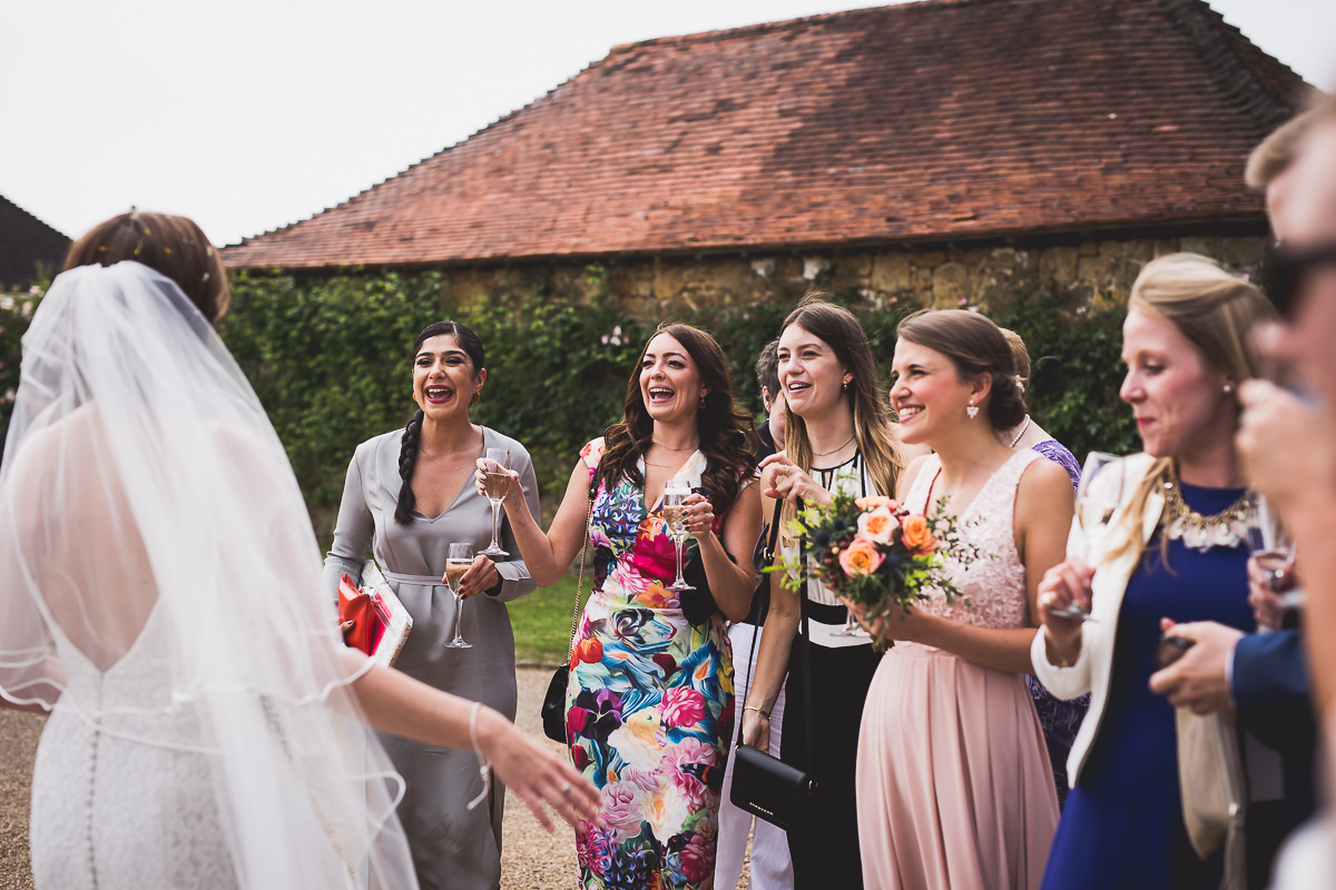 A group of bridesmaids laughing in front of a barn during a wedding photoshoot.