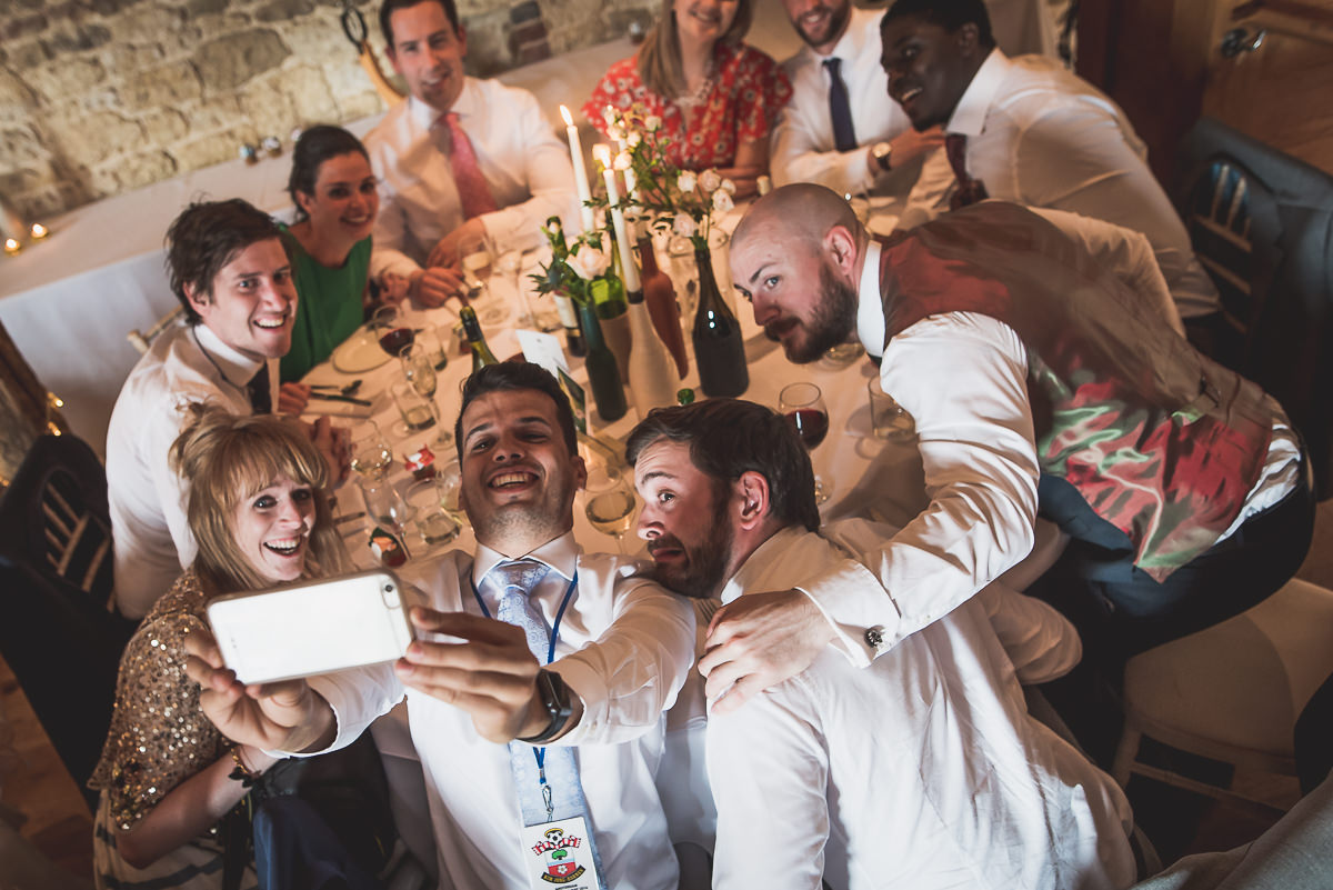 A bride and wedding photographer capturing a group selfie at a wedding.