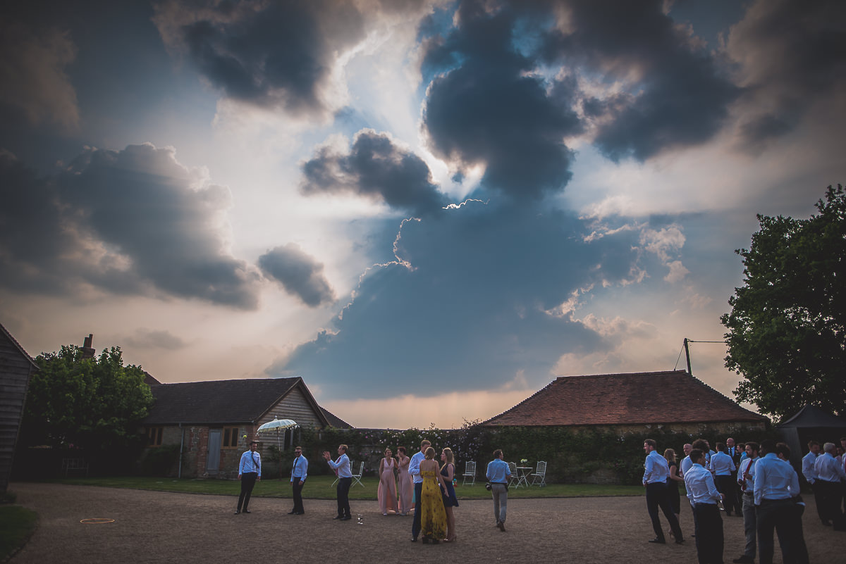 A bride and groom standing in front of a barn under a cloudy sky.