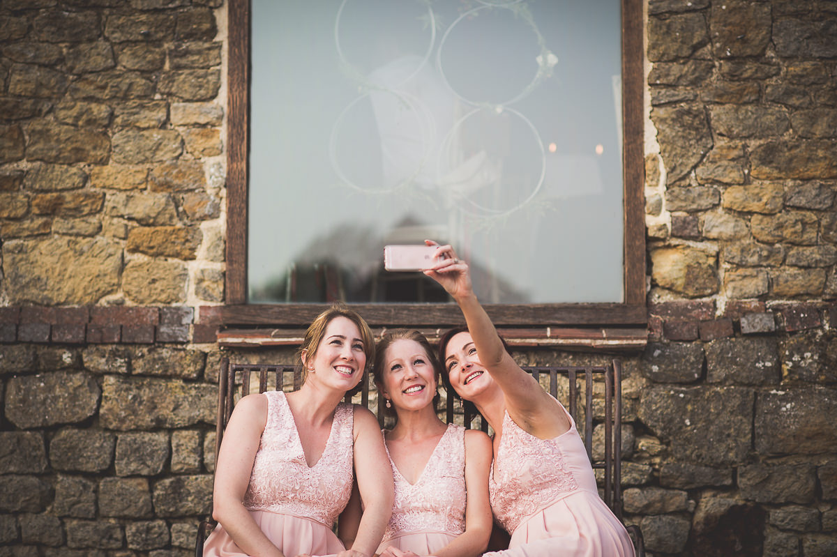 Three bridesmaids posing for a wedding photo in front of a stone wall.