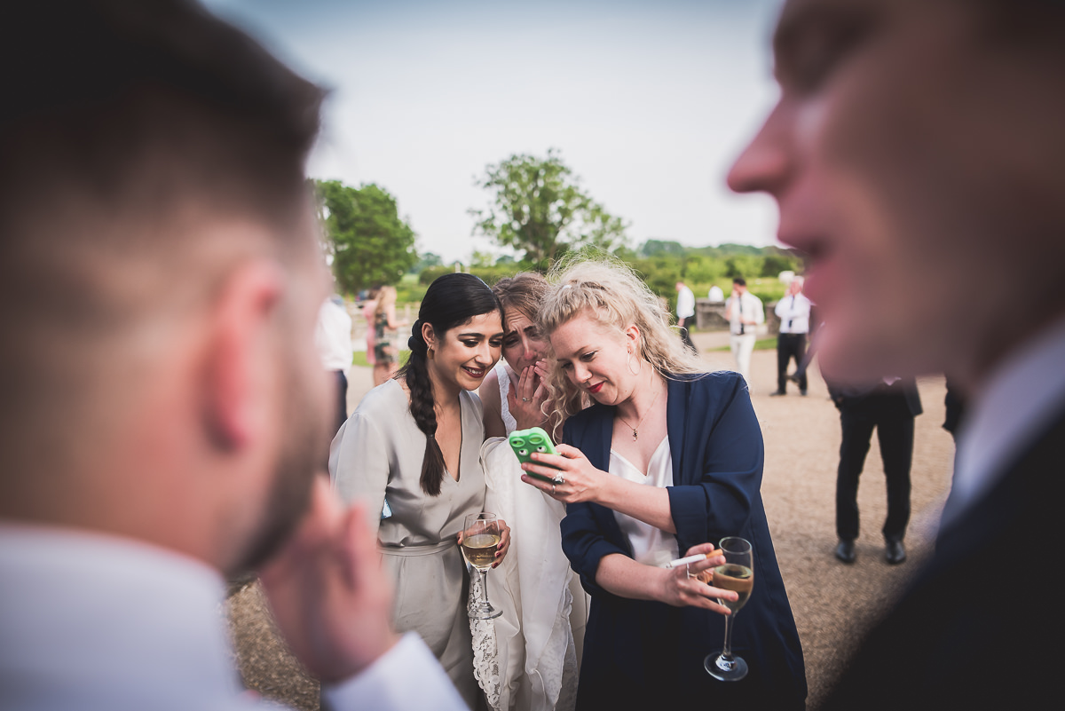 A group of people at a wedding, including the bride, captivated by a cell phone.