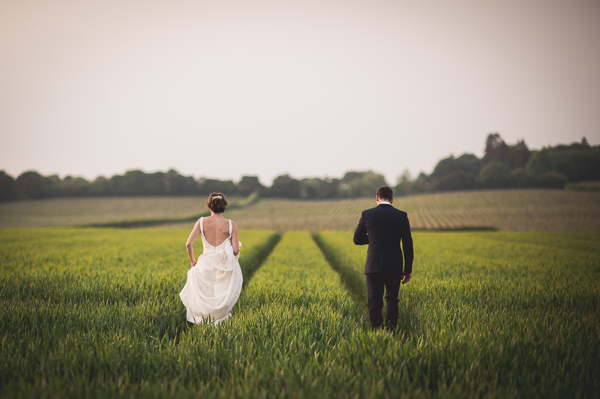 A wedding photograph capturing a bride and groom strolling through a field.