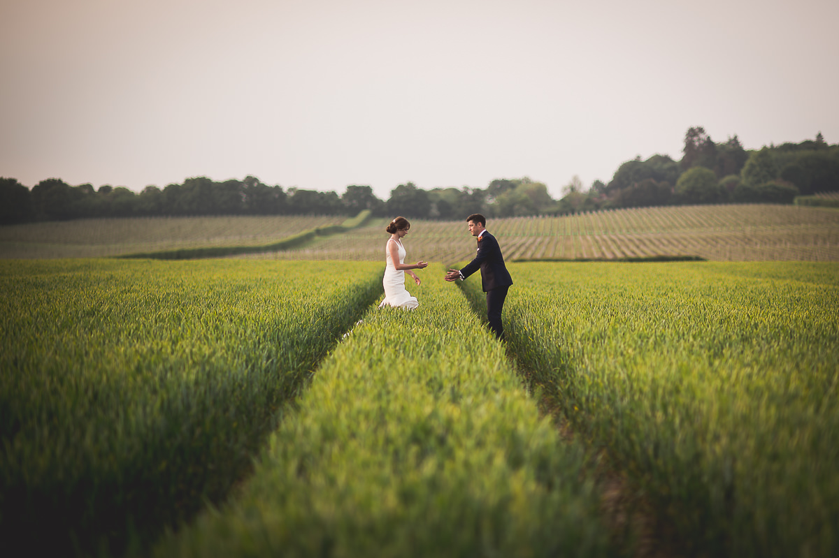 A wedding photographer captures the groom standing in a field on his special day.