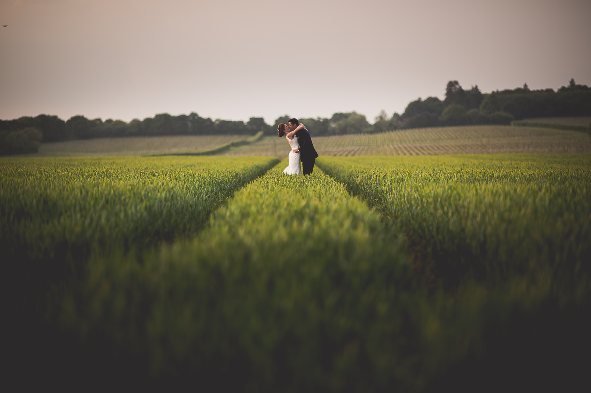 A wedding photographer captures a romantic moment between the bride and groom in a field.