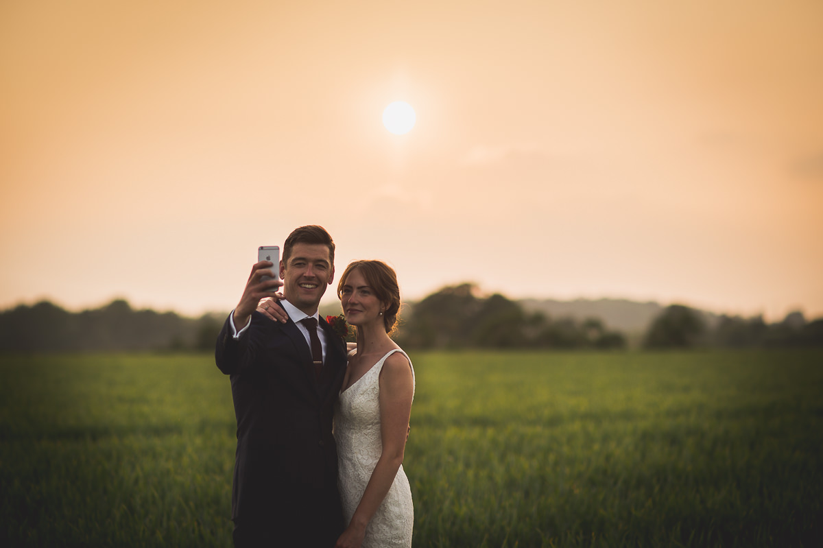 A newlywed couple capturing a selfie in a picturesque field.