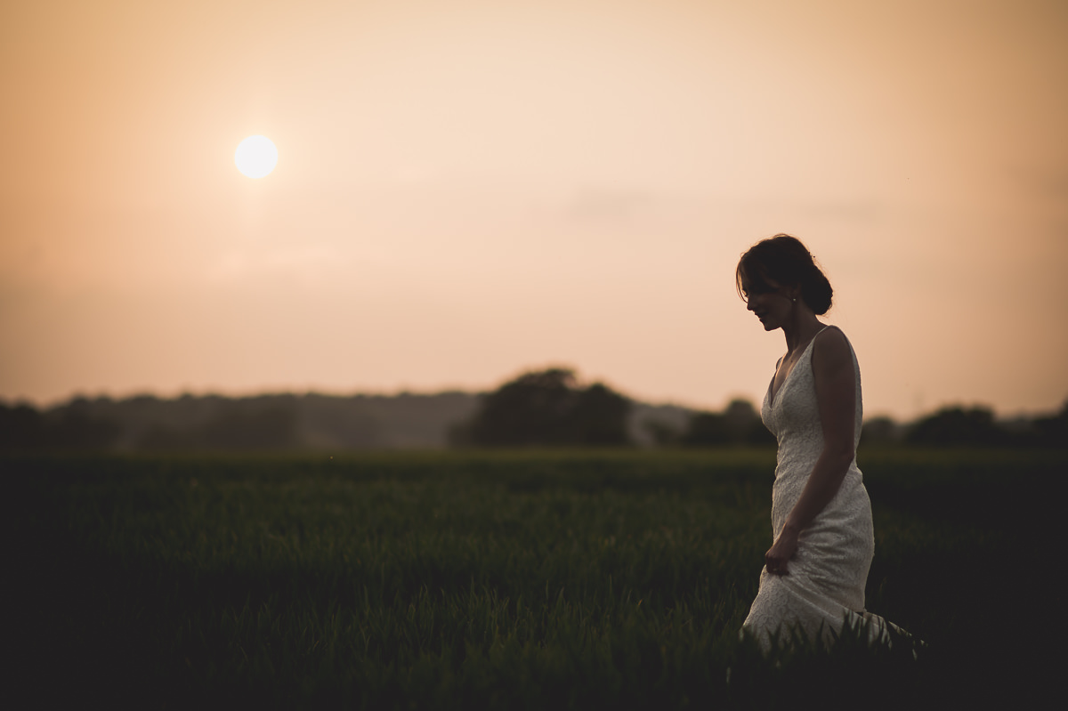 A bride being photographed by a wedding photographer in a field at sunset.