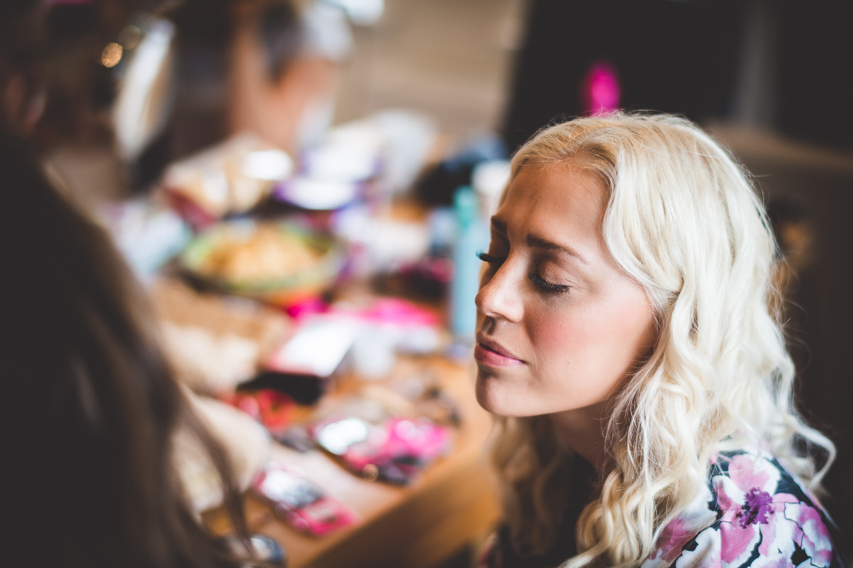 A bride is getting her makeup done at a table for her wedding photo.