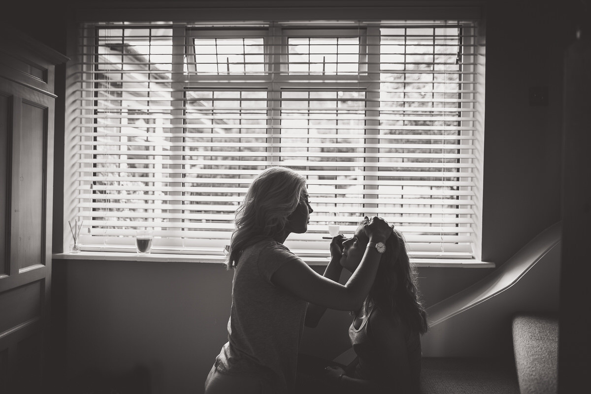 A bride is being groomed for her wedding photo by a wedding photographer in front of a window.