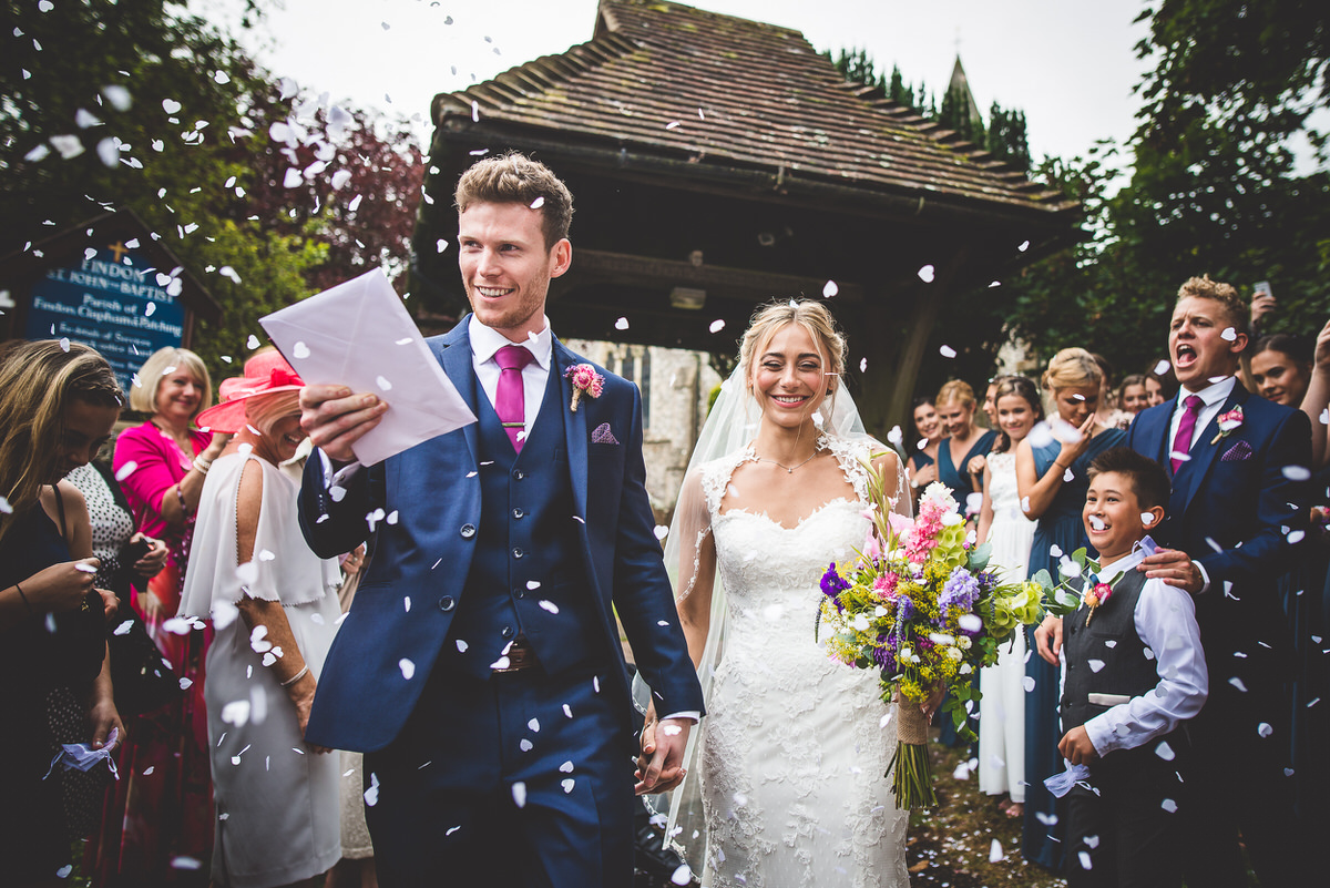 A groom and bride, captured by a wedding photographer, walk down the aisle amidst confetti.