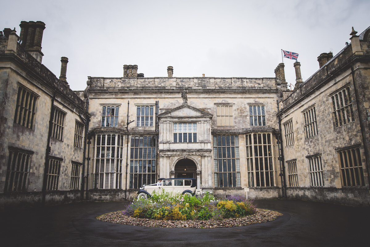 A wedding photographer captures a car parked in front of a large building for the bride and groom.