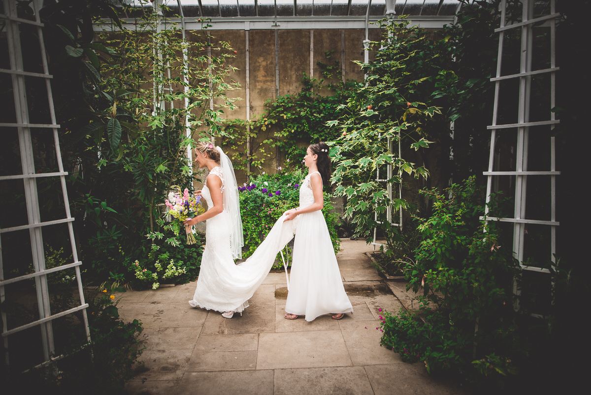 Two brides walking through a greenhouse on their wedding day.