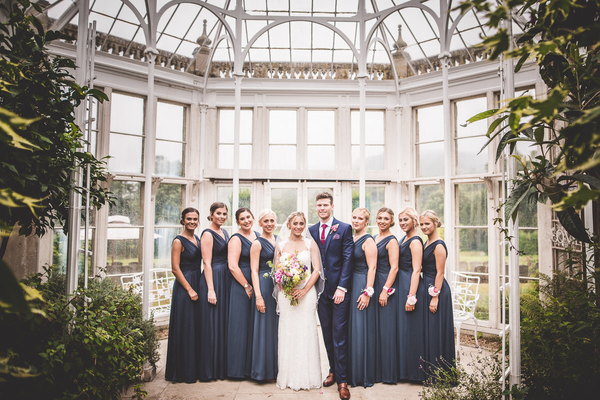 A wedding photographer capturing the bride and wedding party in a conservatory.