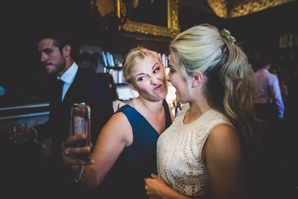 Two women, including the bride, taking a selfie with a wedding photographer at a party.