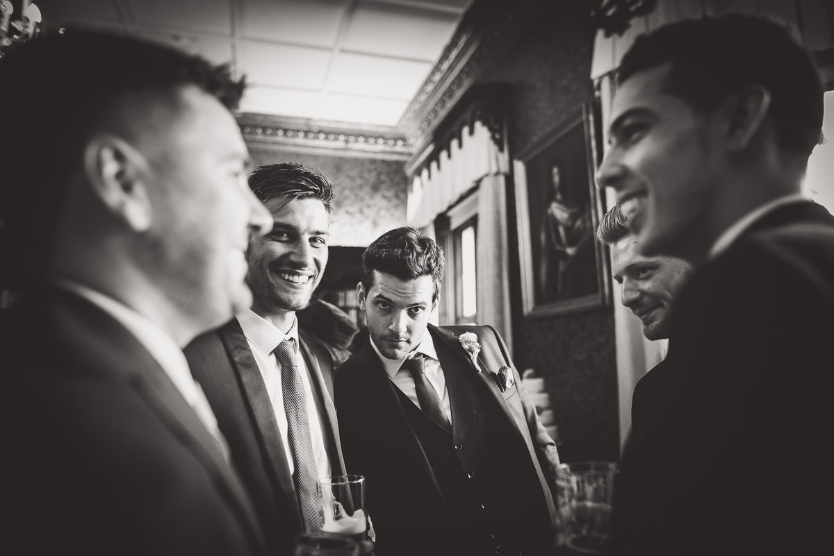 A black and white photo of a group of men laughing at a wedding.