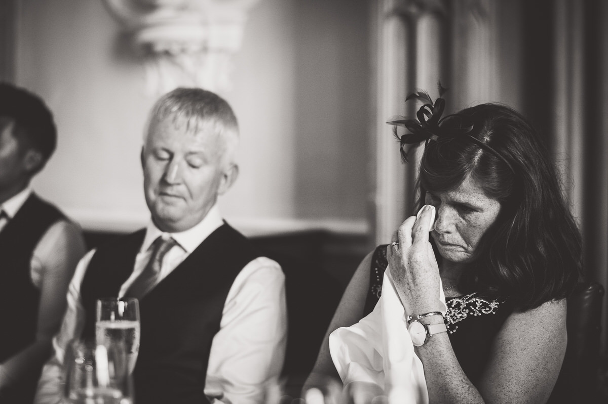 A bride is wiping her eyes while sitting at a table for a wedding photo.