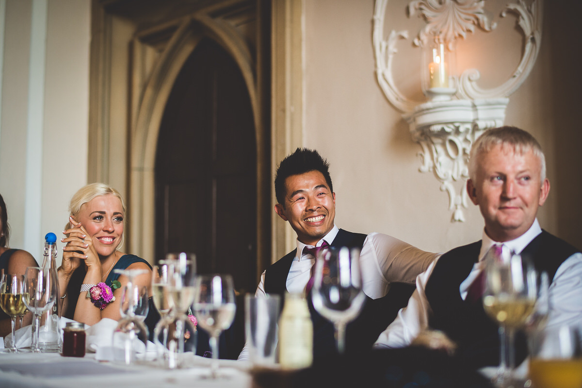 A wedding photo with the bride surrounded by a group of people sitting at a table with glasses of wine.