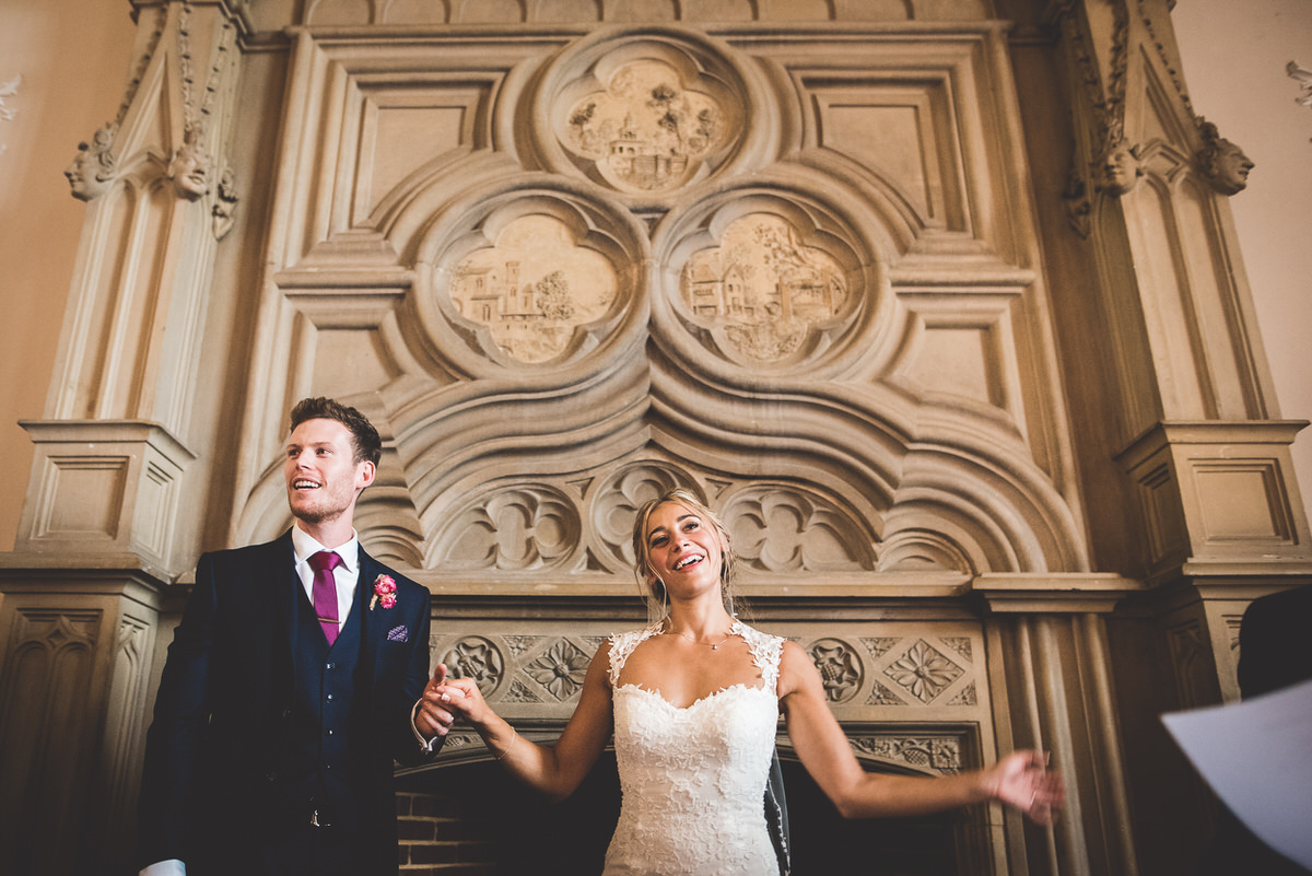 A wedding photographer capturing a bride and groom in front of an ornate fireplace.