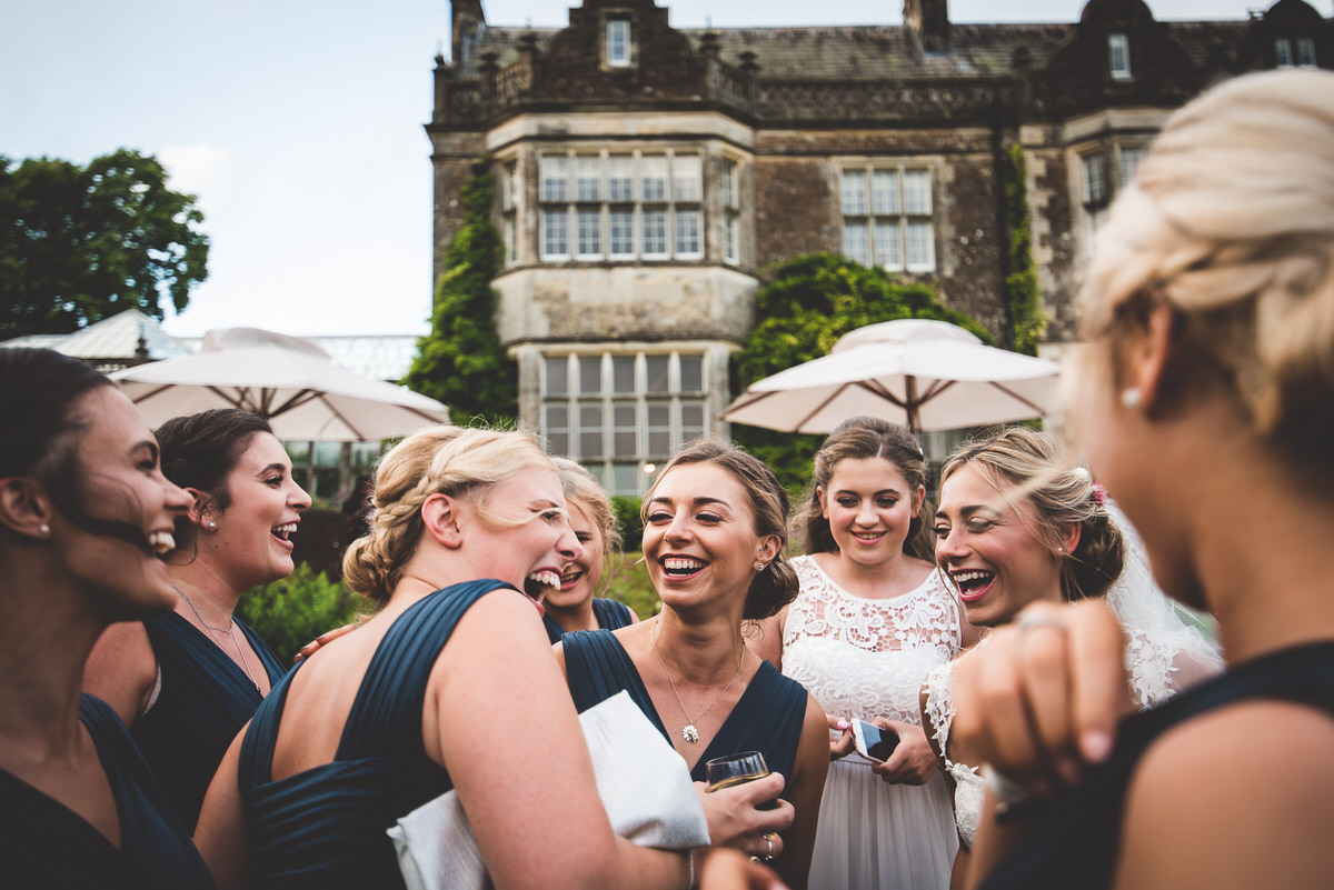 A group of bridesmaids laughing in front of a house during a wedding photo session.