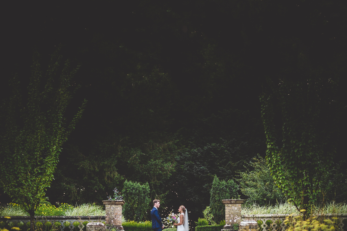 A bride and groom posing for their wedding photo in a dimly lit garden.