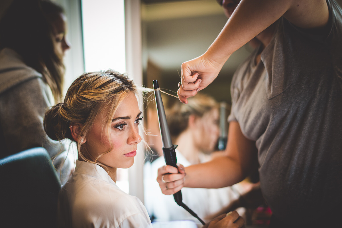 A bride getting her hair done for her wedding in front of a mirror.