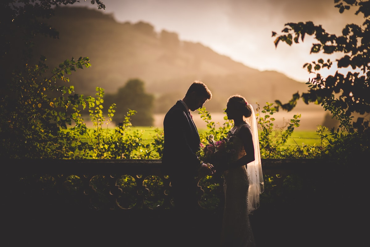 A wedding photographer capturing a bride and groom in a field at sunset.