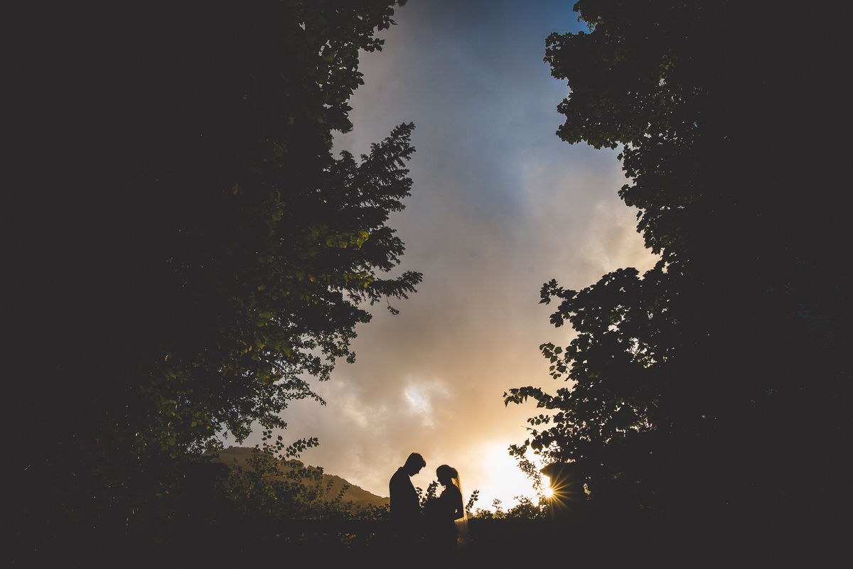A silhouette of a bride and groom in the woods at sunset, captured for their wedding photo.