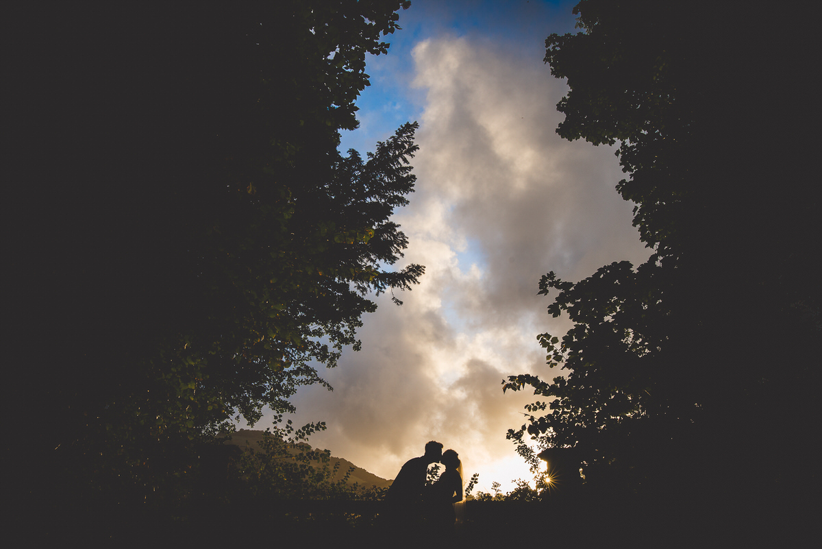 A bride and groom sharing a romantic kiss in the woods at sunset, captured by a wedding photographer.