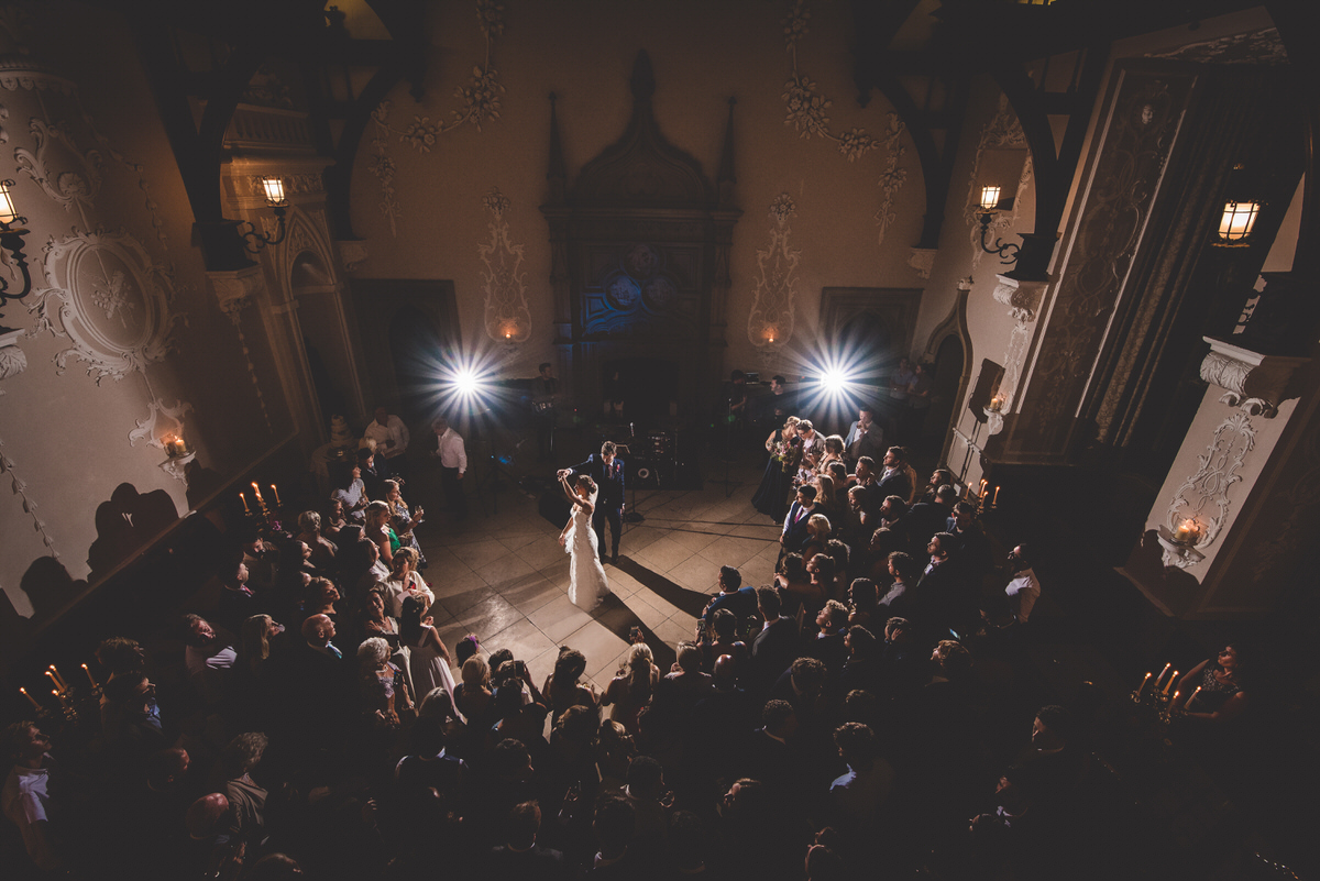 A wedding photographer captures a groom and bride in a dimly-lit room.