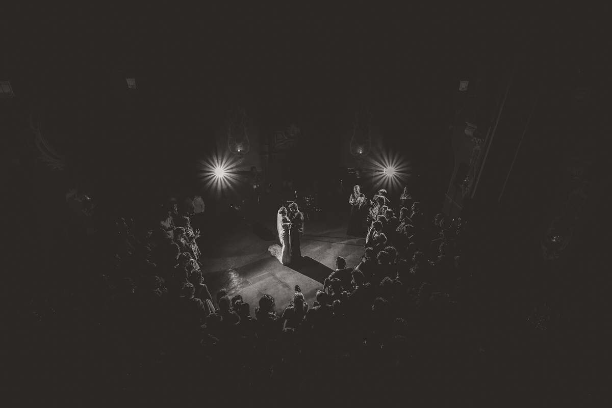 A wedding photographer captures a black and white photo of a bride and groom in a dark room.