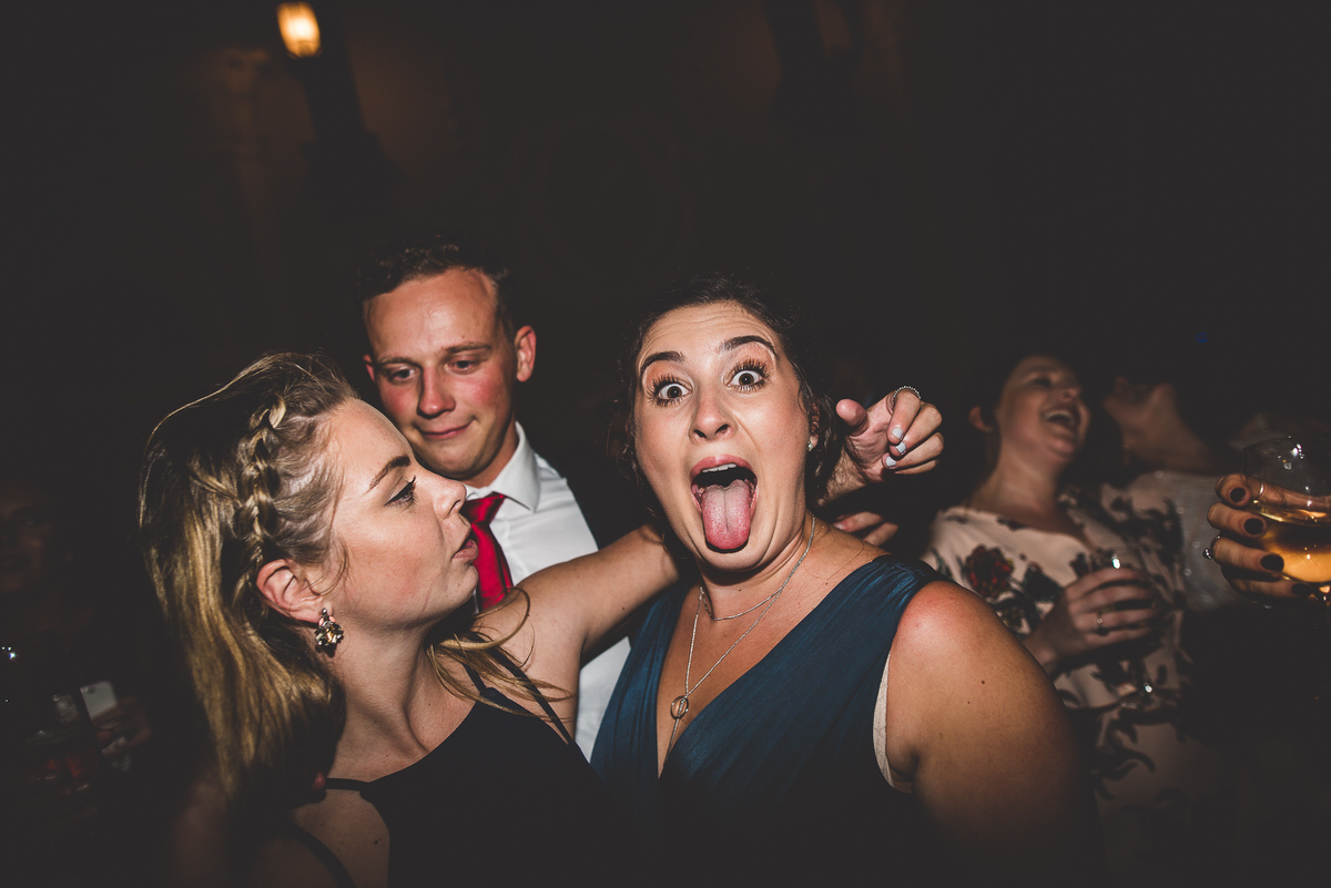A bride and groom surrounded by a group of people with tongues out at their wedding party.