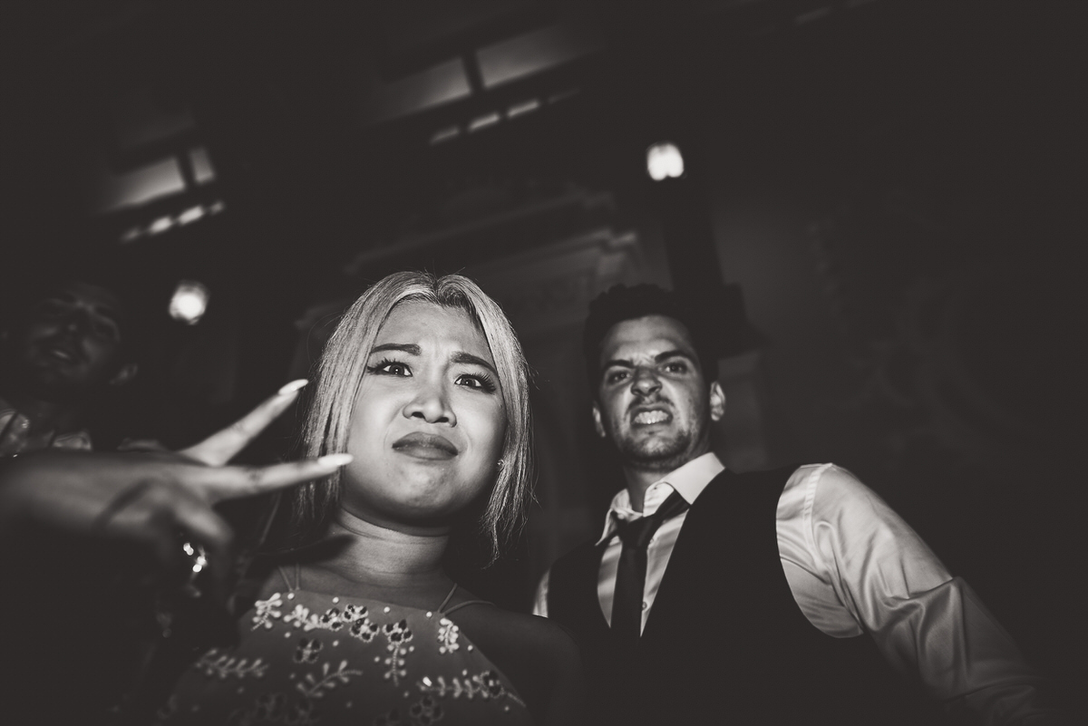 A groom and a bride making a hand gesture in front of a wedding crowd.