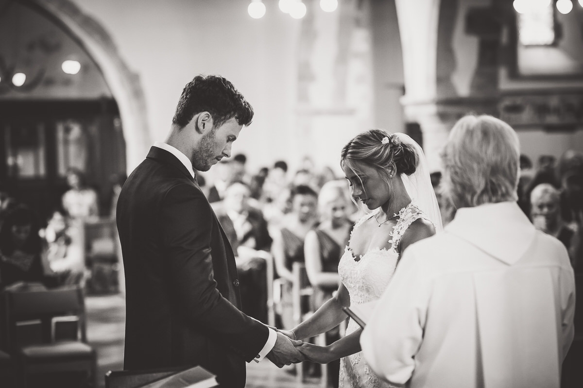 A bride and groom say their vows during a wedding ceremony in a church while being photographed.