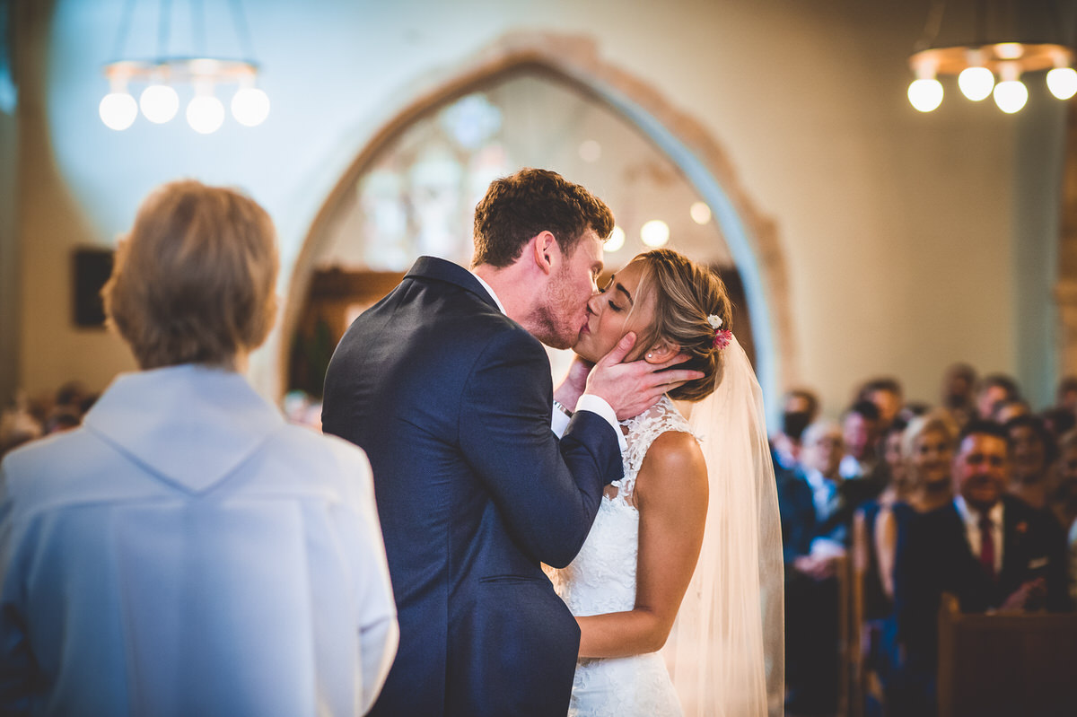 A wedding photographer captures a passionate kiss between the bride and groom during their ceremony.