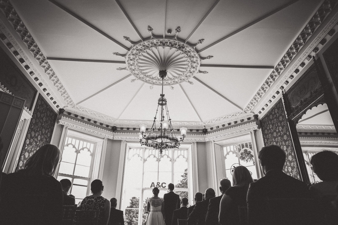 A black and white wedding photo capturing the groom during a ceremony in an ornate room.