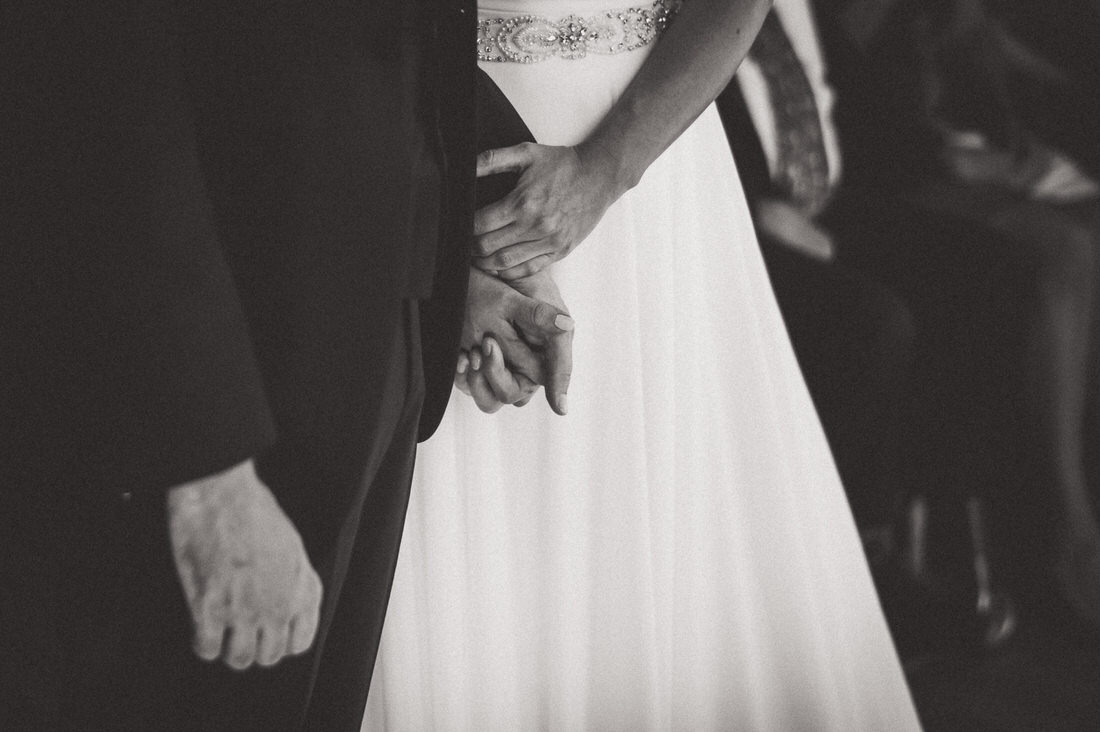A black and white wedding photo capturing the bride and groom holding hands.