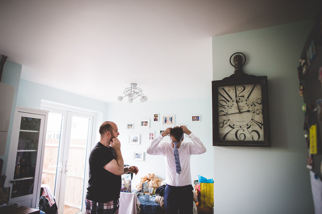 A groom is preparing for his wedding photo in a room with a clock.