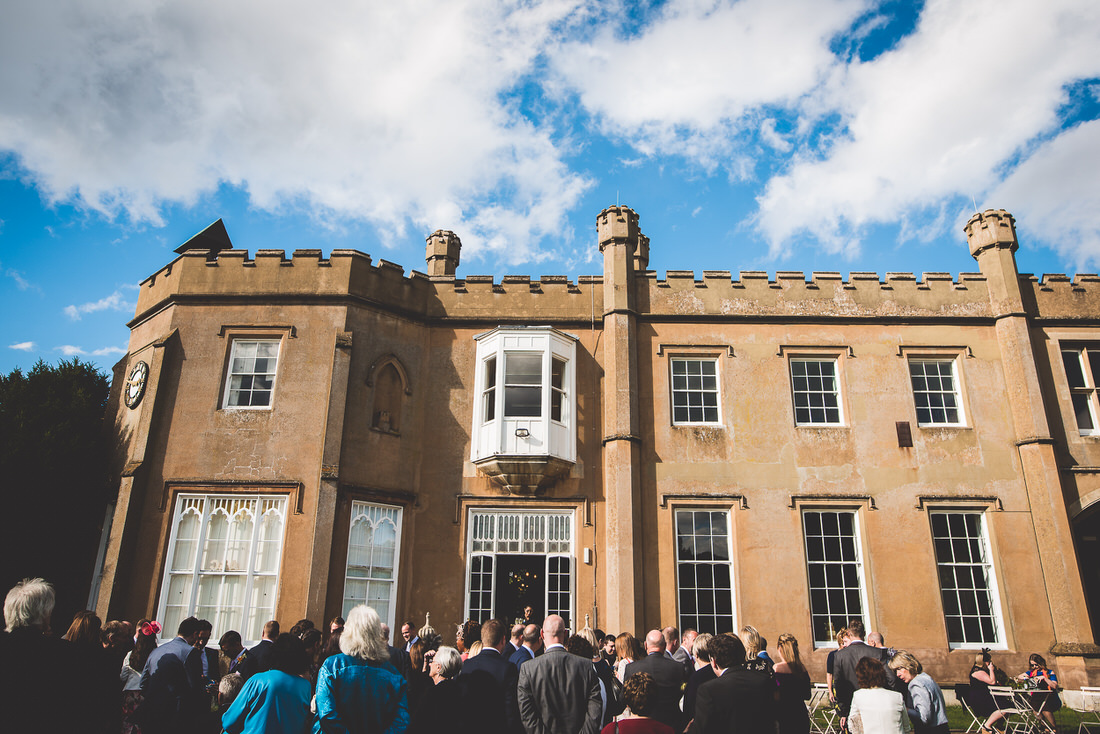A wedding photo, with the groom and a group of people standing in front of a castle.