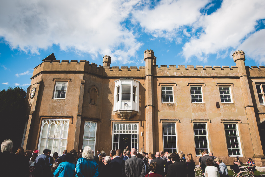 A wedding photo, with the groom and a group of people standing in front of a castle.