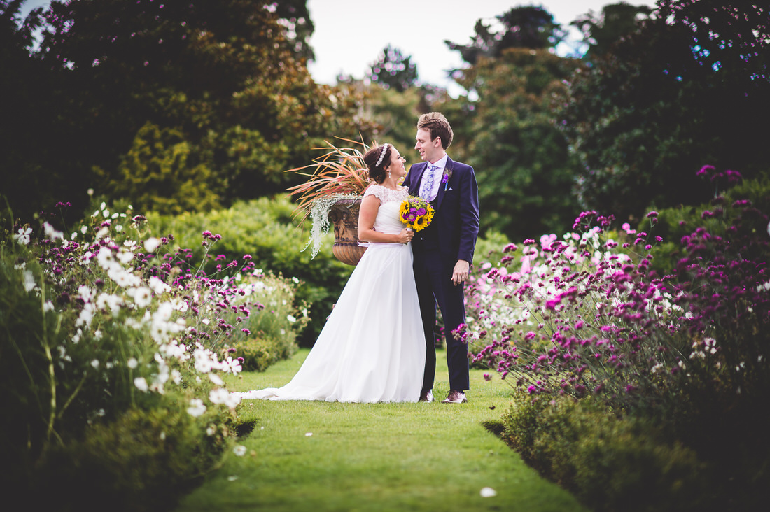 A wedding photographer capturing a bride and groom in a garden.