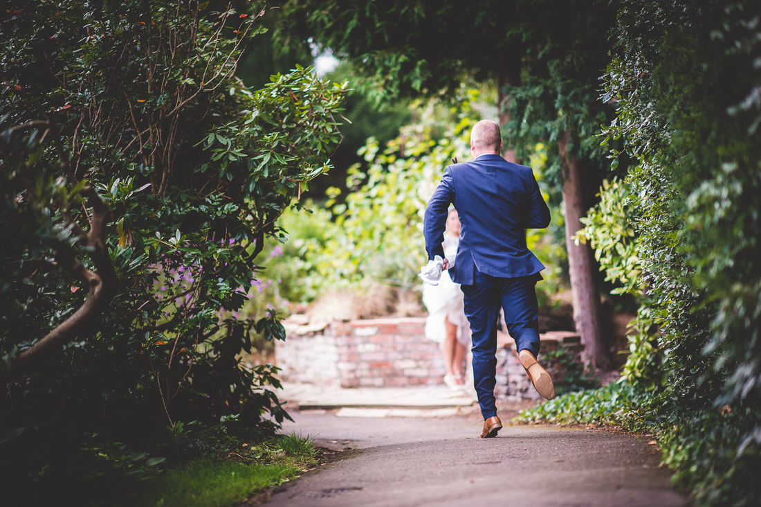 A groom and bride photographed by a wedding photographer running down a path.