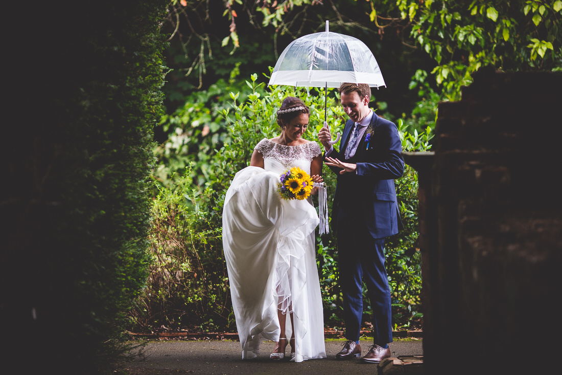 A wedding photographer captures a bride and groom under an umbrella.