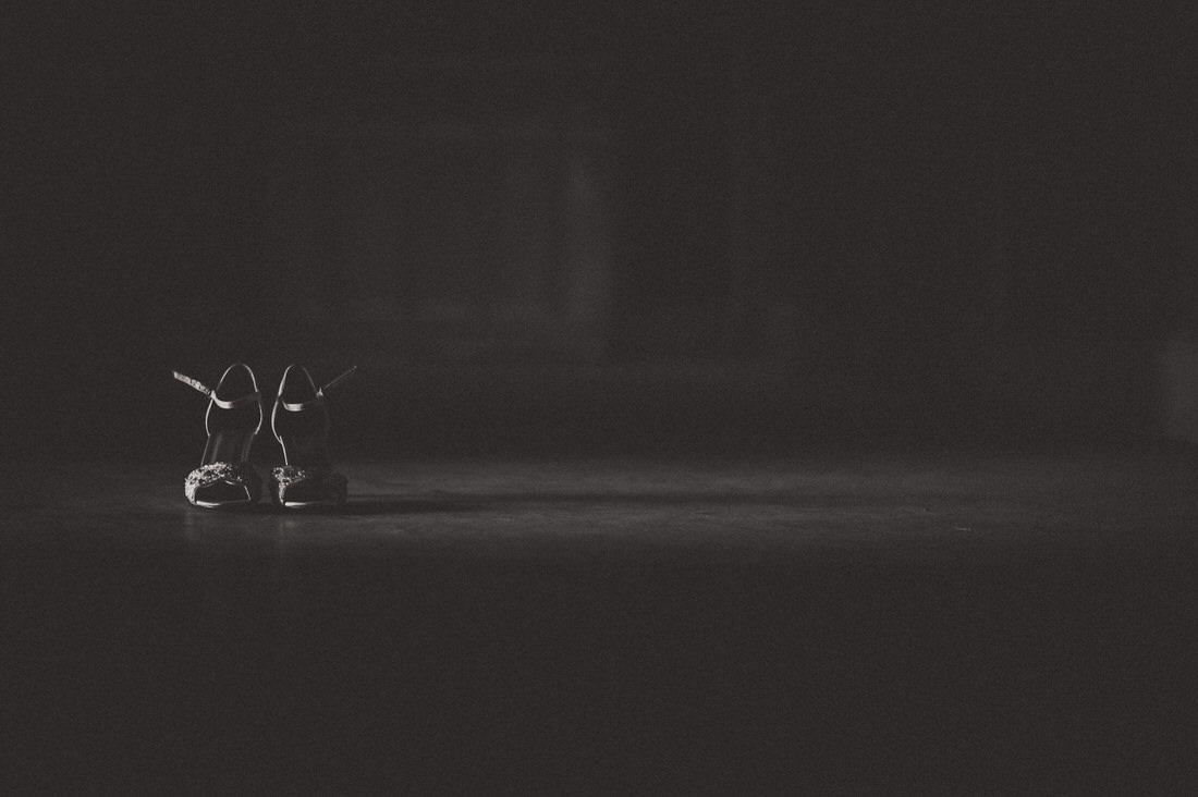 A black and white wedding photo of the groom's shoes in a dark room.