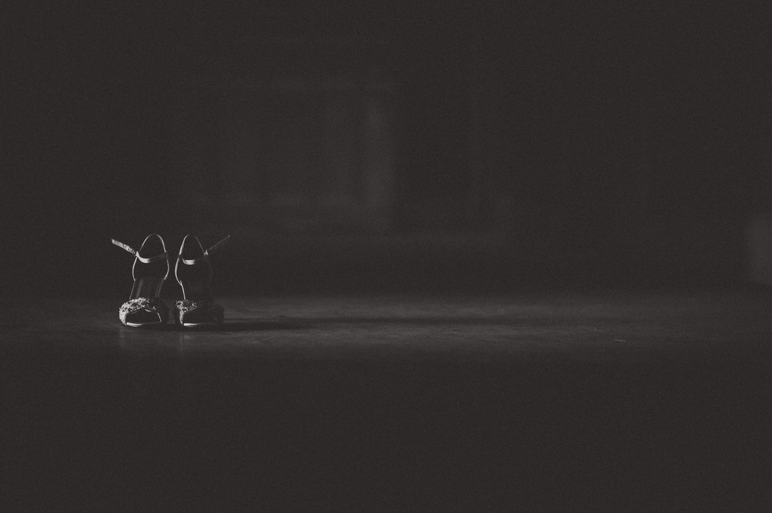 A black and white wedding photo of the groom's shoes in a dark room.