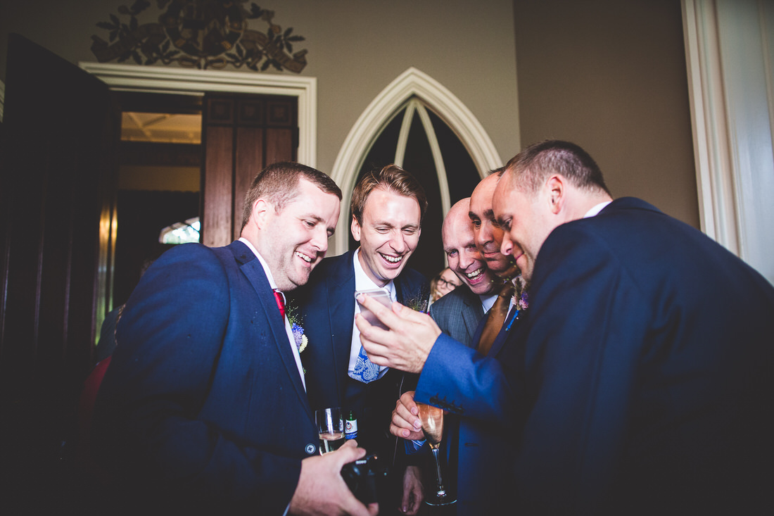 A group of men laughing while capturing a wedding photo.