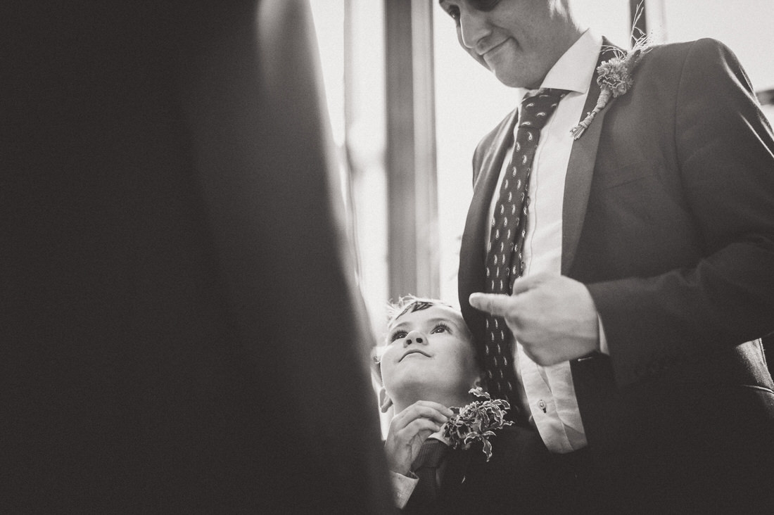 A wedding photographer captures a man in a suit adjusting a boy's tie during the bride's special day.