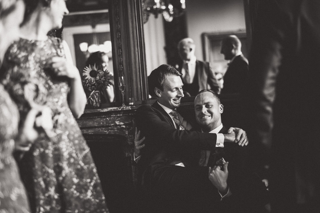 A black and white wedding photo of a groom embracing another man.